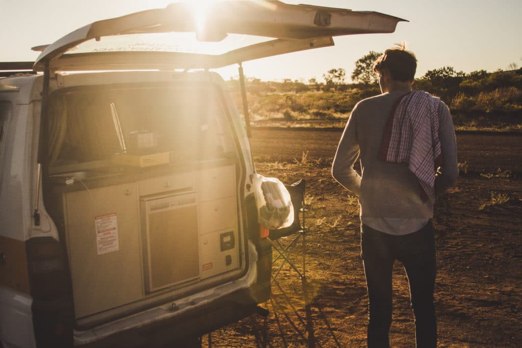 Jeune homme qui a loué un van en Australie et prépare à manger à l'arrière du véhicule