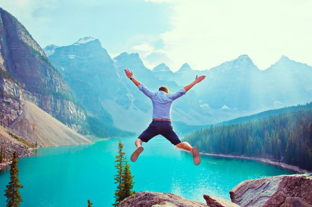 homme qui saute en l'air. enface d'un lac. Il est content car il est parti bien assuré pour son voyage à l'étranger