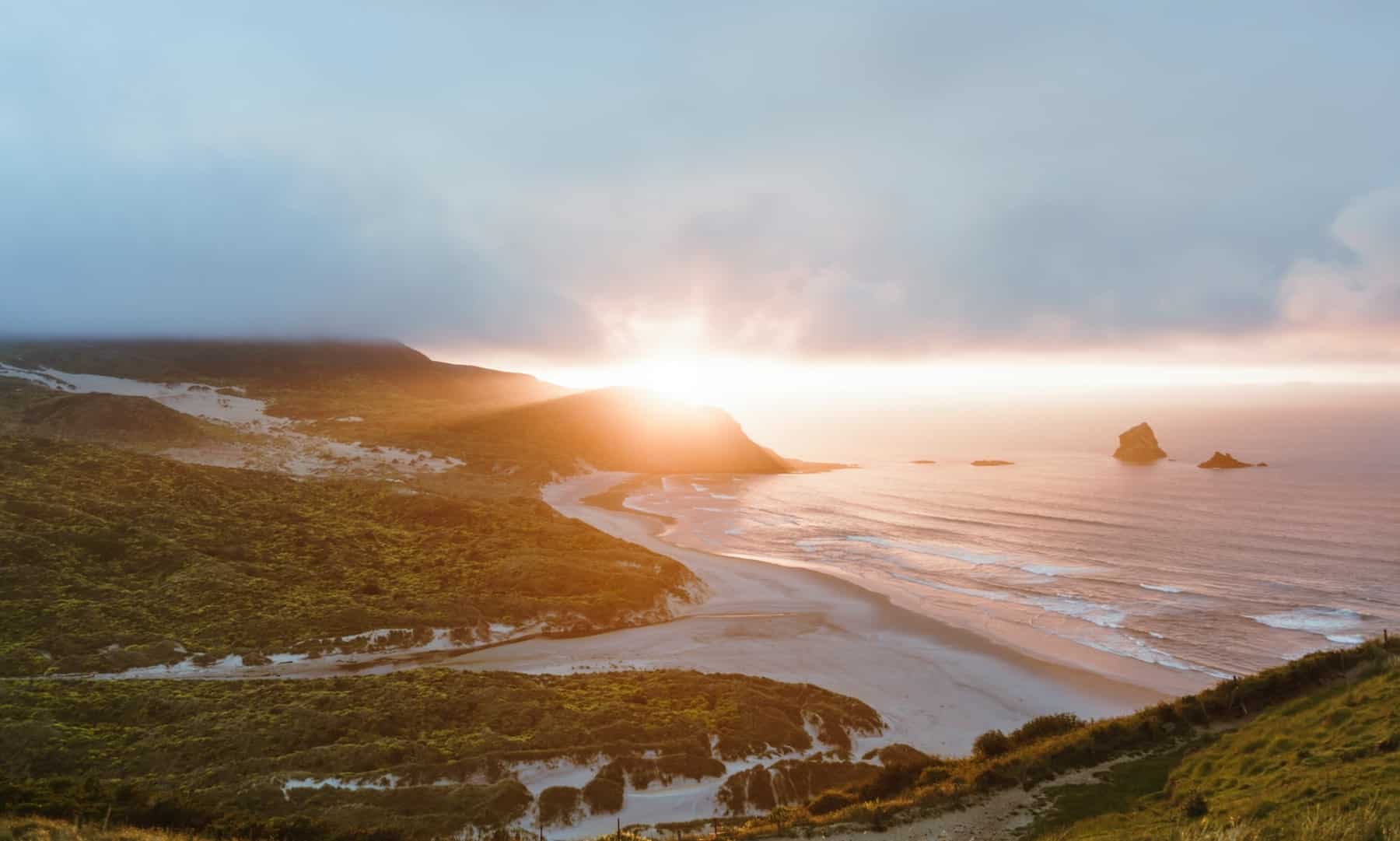 soleil levant sur une plage de nouvelle zélande, admiré depuis sa location de van pas cher