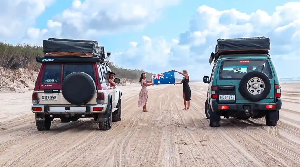 2 voitures 4x4 sur une plage de Fraser Island avec deux filles au milieu tenant le drapeau de l'Australie